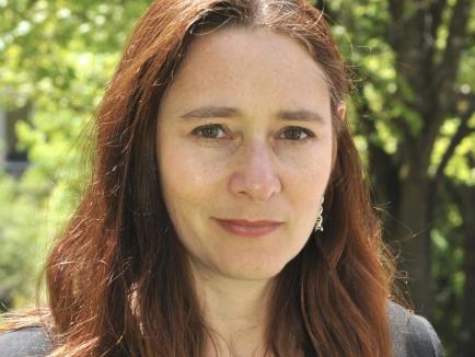 A woman with brown hair stands outside looking at the camera