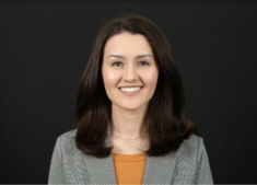 Charlier Fisher in front of a black background with an orange shirt and gray blazer.