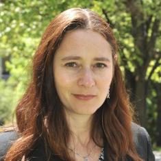 A woman with brown hair stands outside looking at the camera